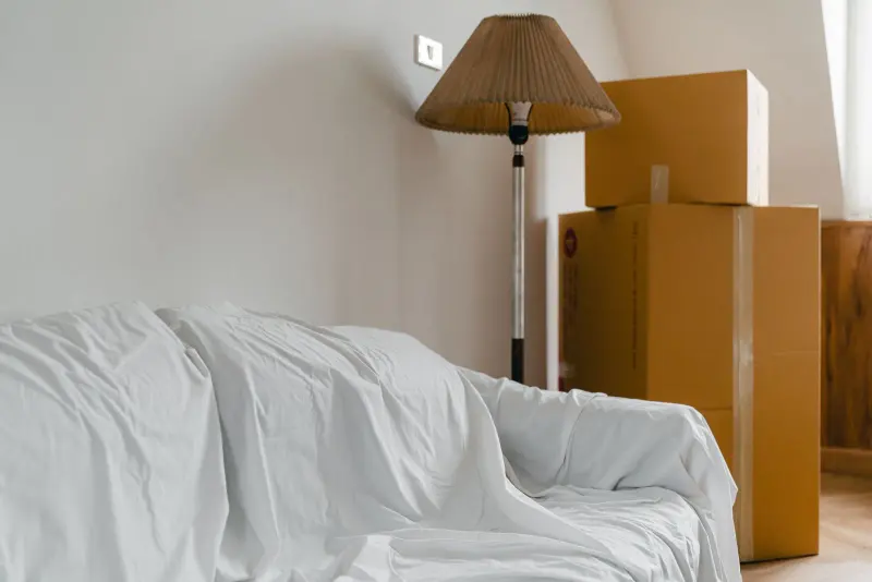 Sofa under a dust sheet and packed boxes in a light room